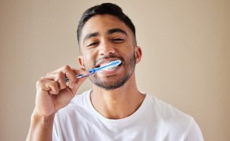 Man smiling while brushing his teeth