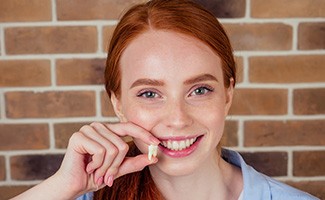 A red-headed woman holding her extracted tooth 