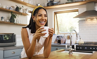 Woman smiling while drinking coffee in kitchen