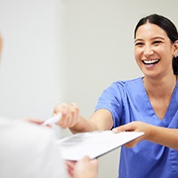 Woman handing forms and pen to staff in blue scrubs