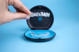 Someone lifting an Invisalign tray out of its carrier case with a blue background